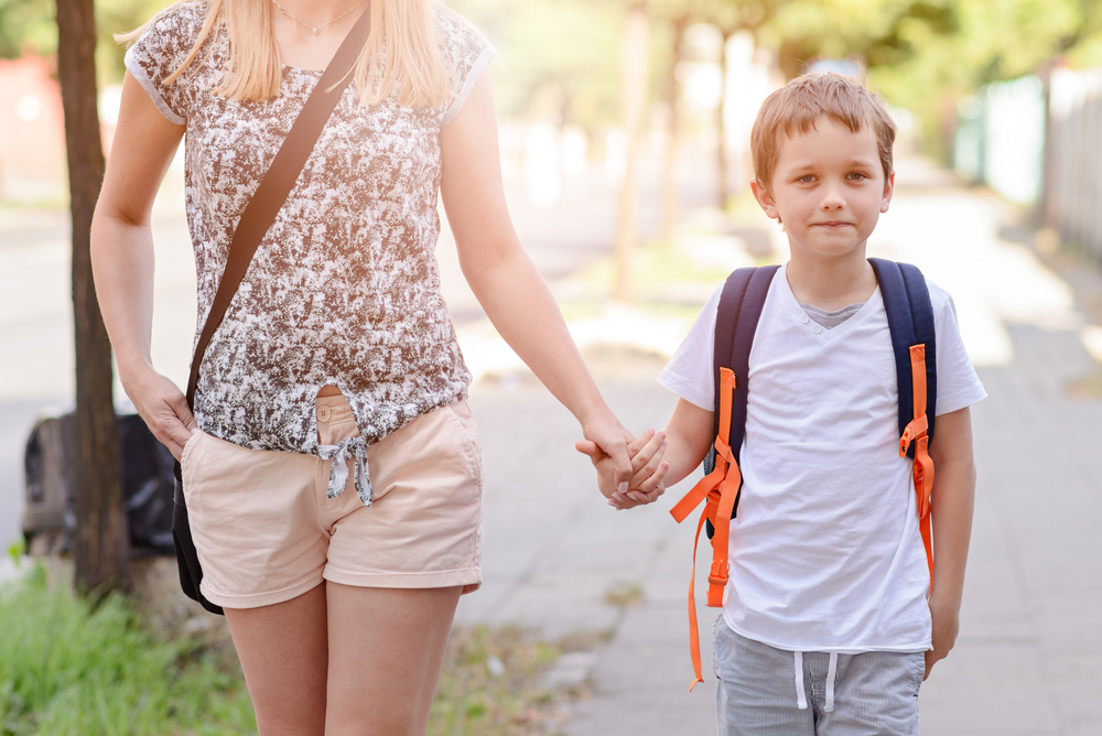 Garoto em transição para o Ensino Fundamental segurando a mão de sua mãe, a caminho da escola